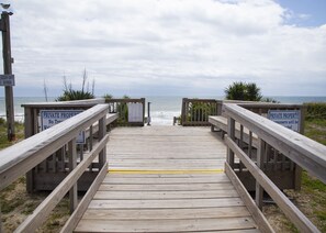 A wooden boardwalk leading to the beach with 'PRIVATE PROPERTY' signs and a 'KEEP OFF DUNES' sign.