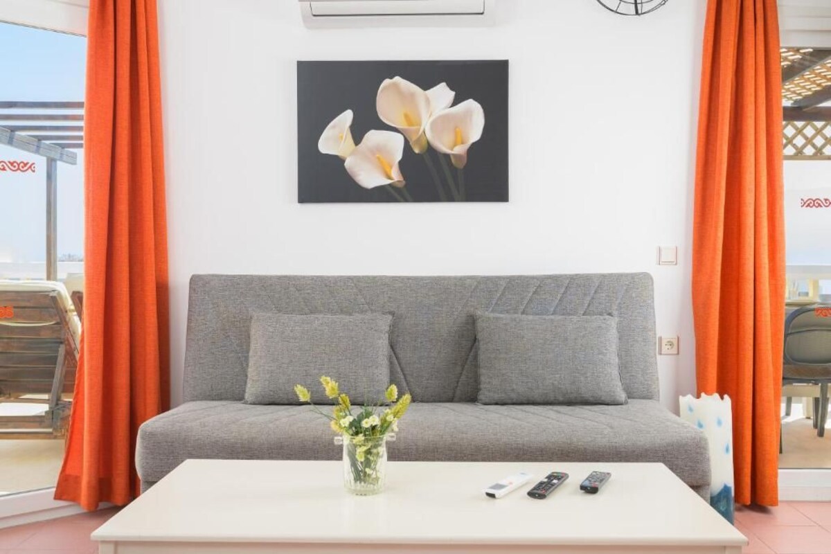 Ein graues Sofa mit zwei Kissen, ein weißer Couchtisch mit einer Blumenvase und ein Blumenbild in einem Rahmen an der Wand.