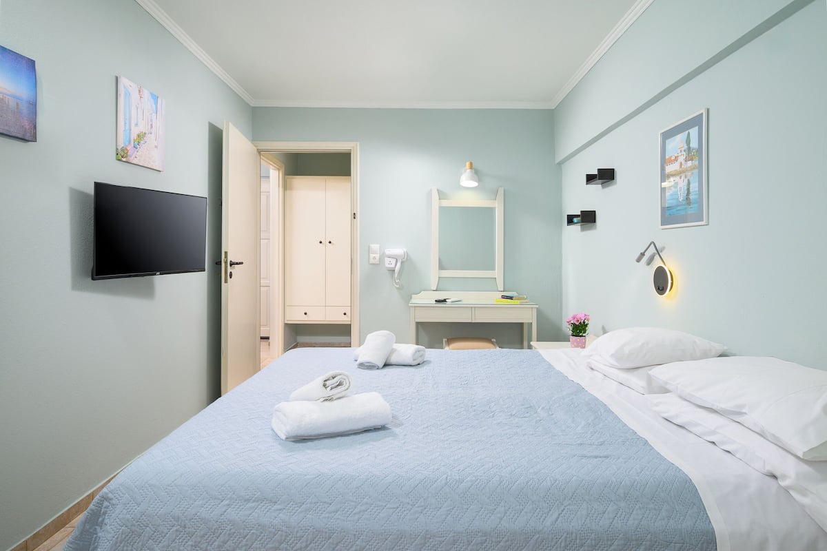A hotel room with a bed, a TV, a desk with a chair, a mirror, and artwork on the walls.