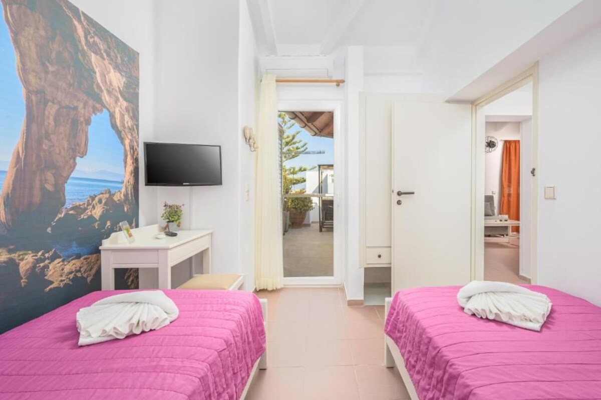 A hotel room with two beds, a TV, a desk, and a painting of a rocky landscape.