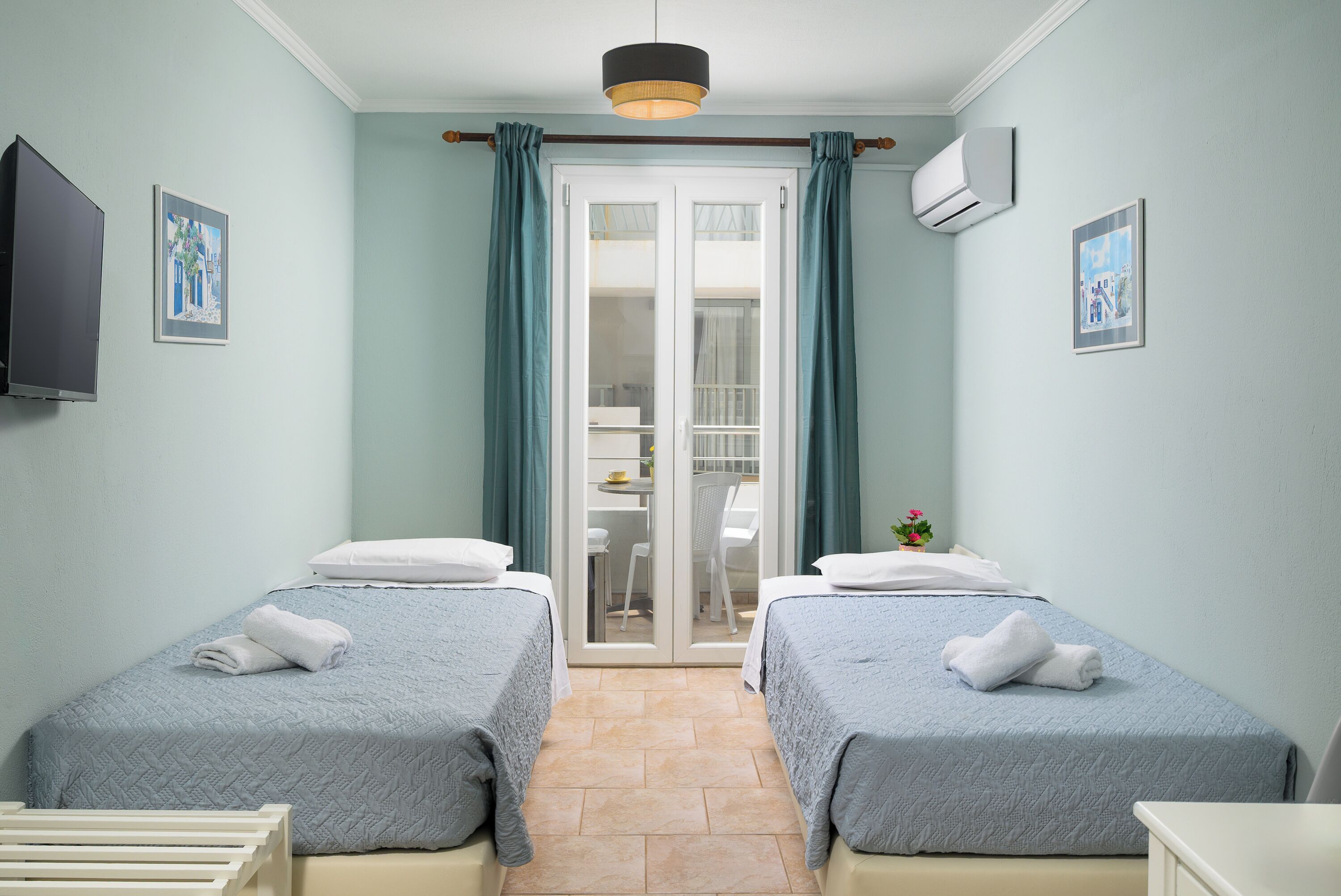 Habitación con dos camas, televisión y puerta corrediza que da a un balcón.