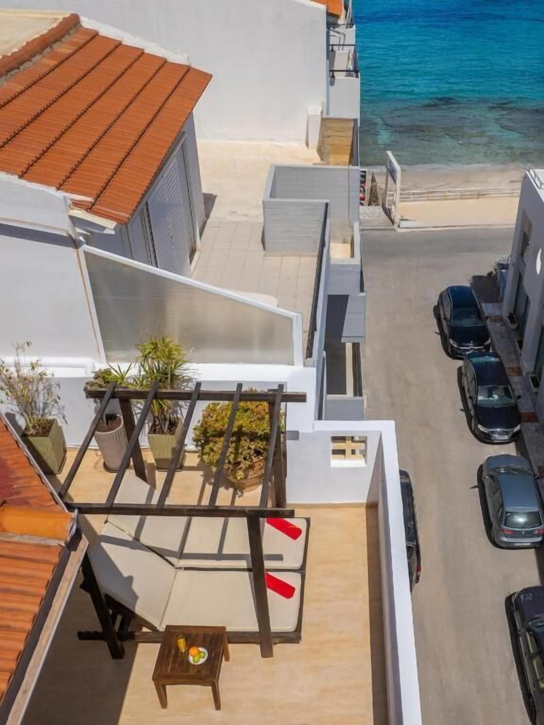 A rooftop terrace with a table, chairs, potted plants, and a view of the sea.