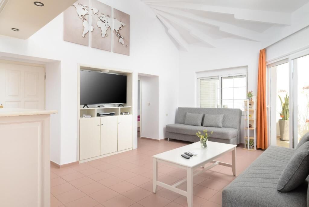 Una sala de estar moderna con un sofá gris, una mesa de centro blanca y un televisor de pantalla plana sobre un mueble blanco.