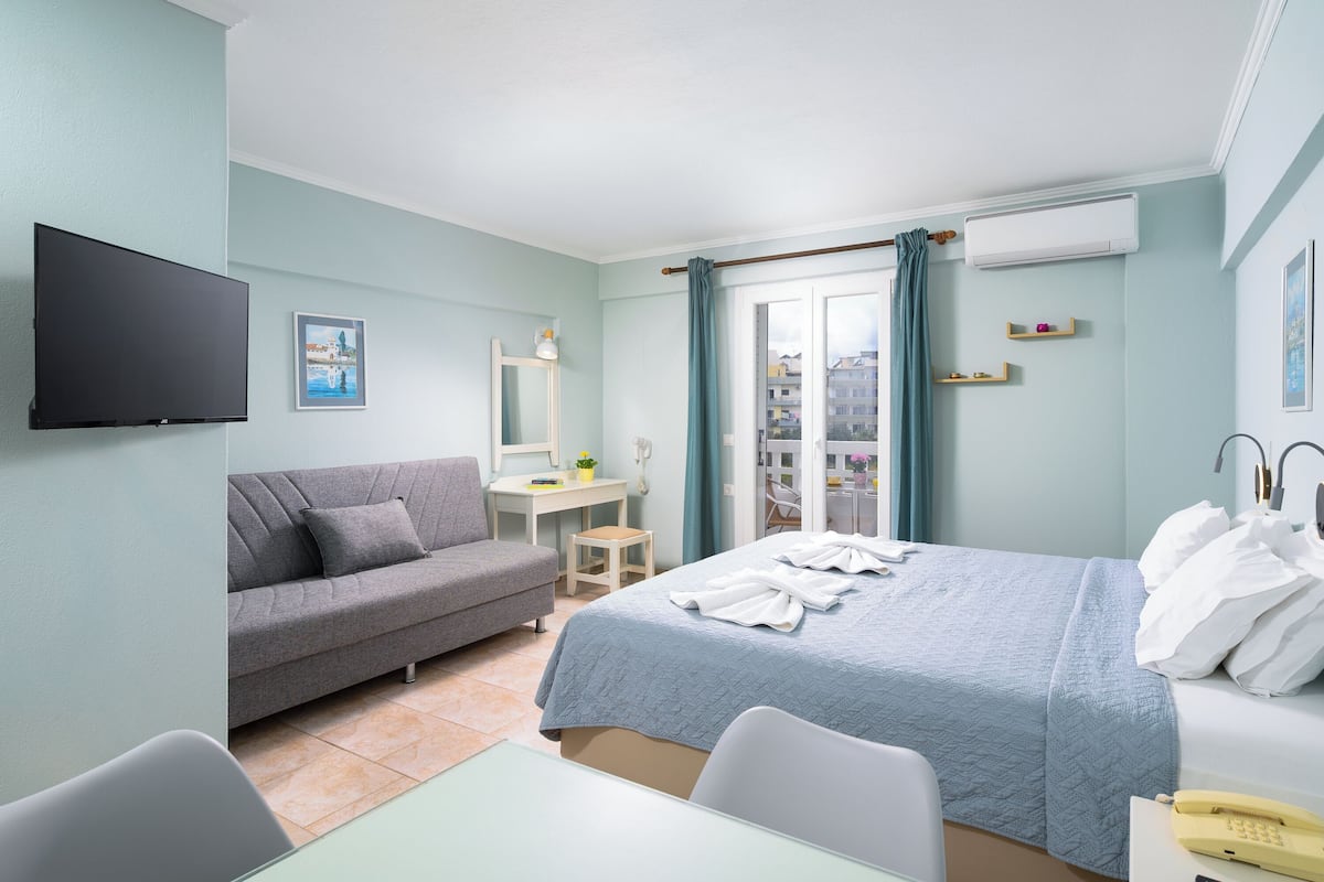 A hotel room with a bed, a sofa, a desk, a television, and a balcony with a view.