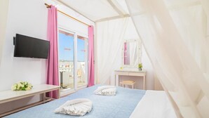 Habitación de hotel con cama, escritorio, televisor, espejo y vistas al exterior.