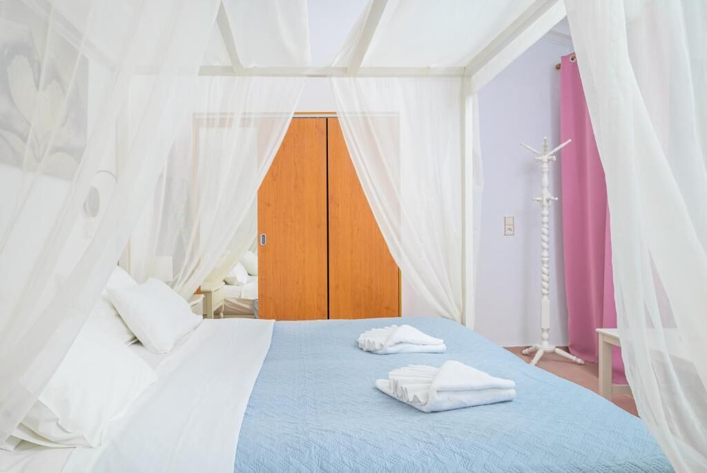 A bedroom with a bed, white curtains, a wooden wardrobe, and a bedside table.