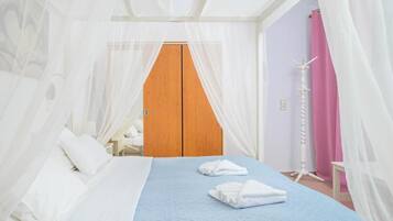 A bedroom with a bed, white curtains, a wooden wardrobe, and a bedside table.