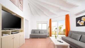 Una sala de estar con sofá, televisión, mesa de centro y ventana con cortinas.