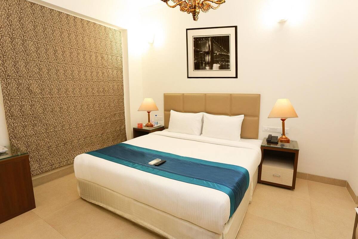 A hotel room with a bed, two bedside tables, a wall with a patterned wallpaper, a framed picture on the wall, and a chandelier.