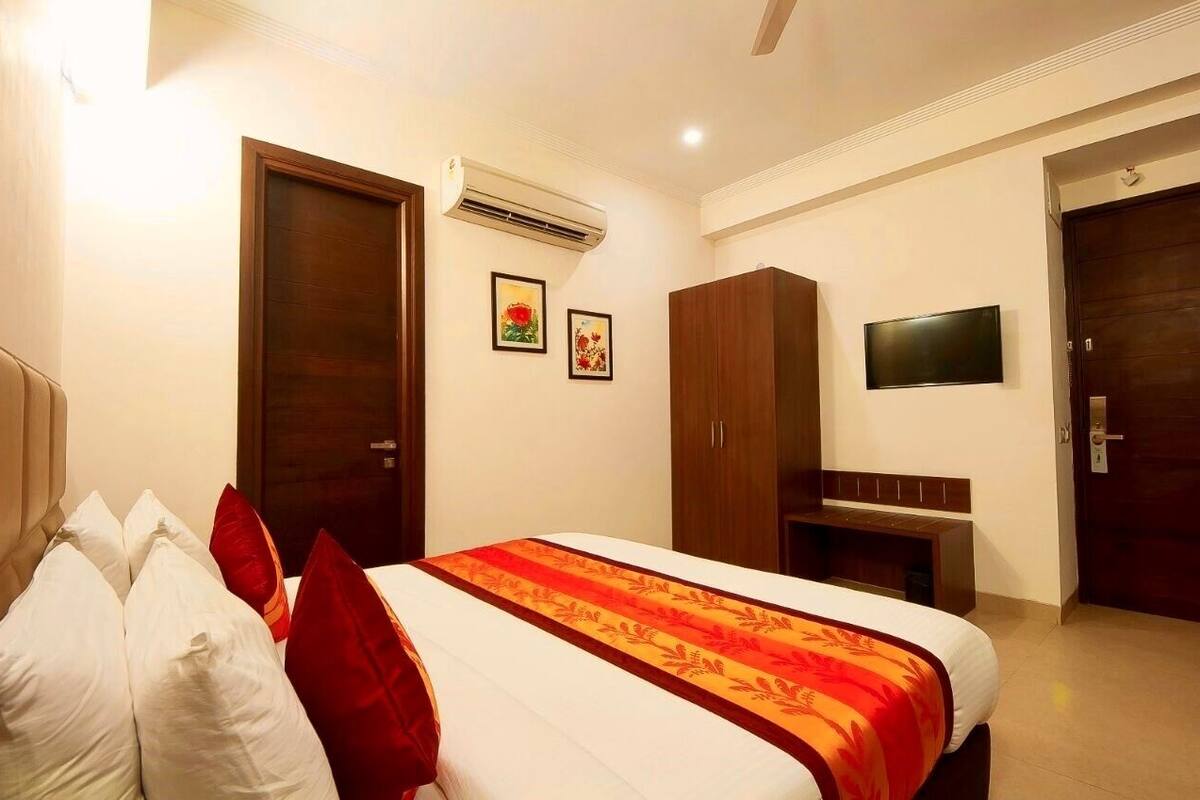 A hotel room with a bed, a wardrobe, a TV mounted on the wall, and an air conditioning unit.