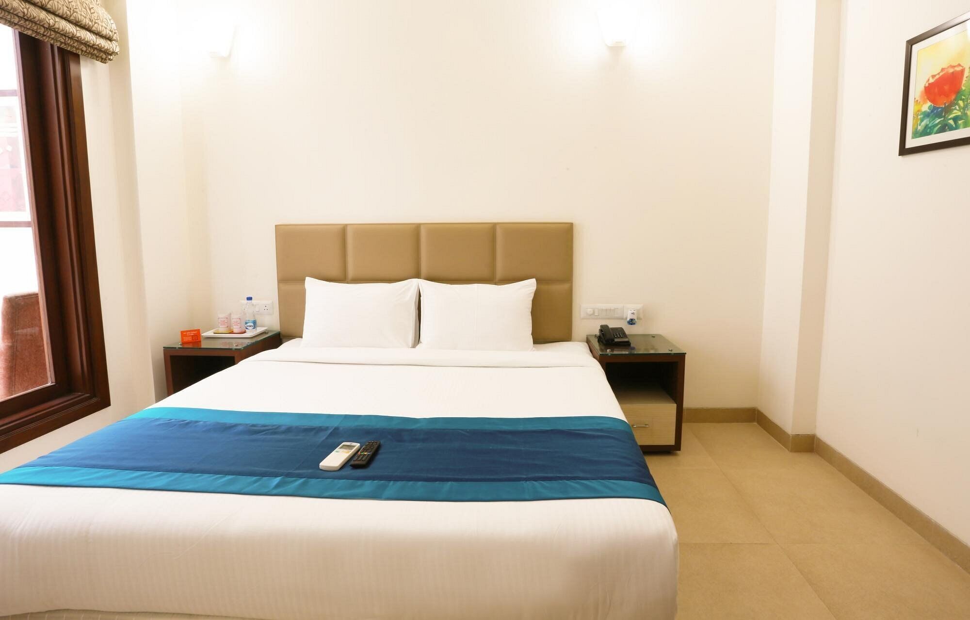 Habitació d'hotel amb llit, una tauleta de nit, un telèfon i un quadre a la paret.