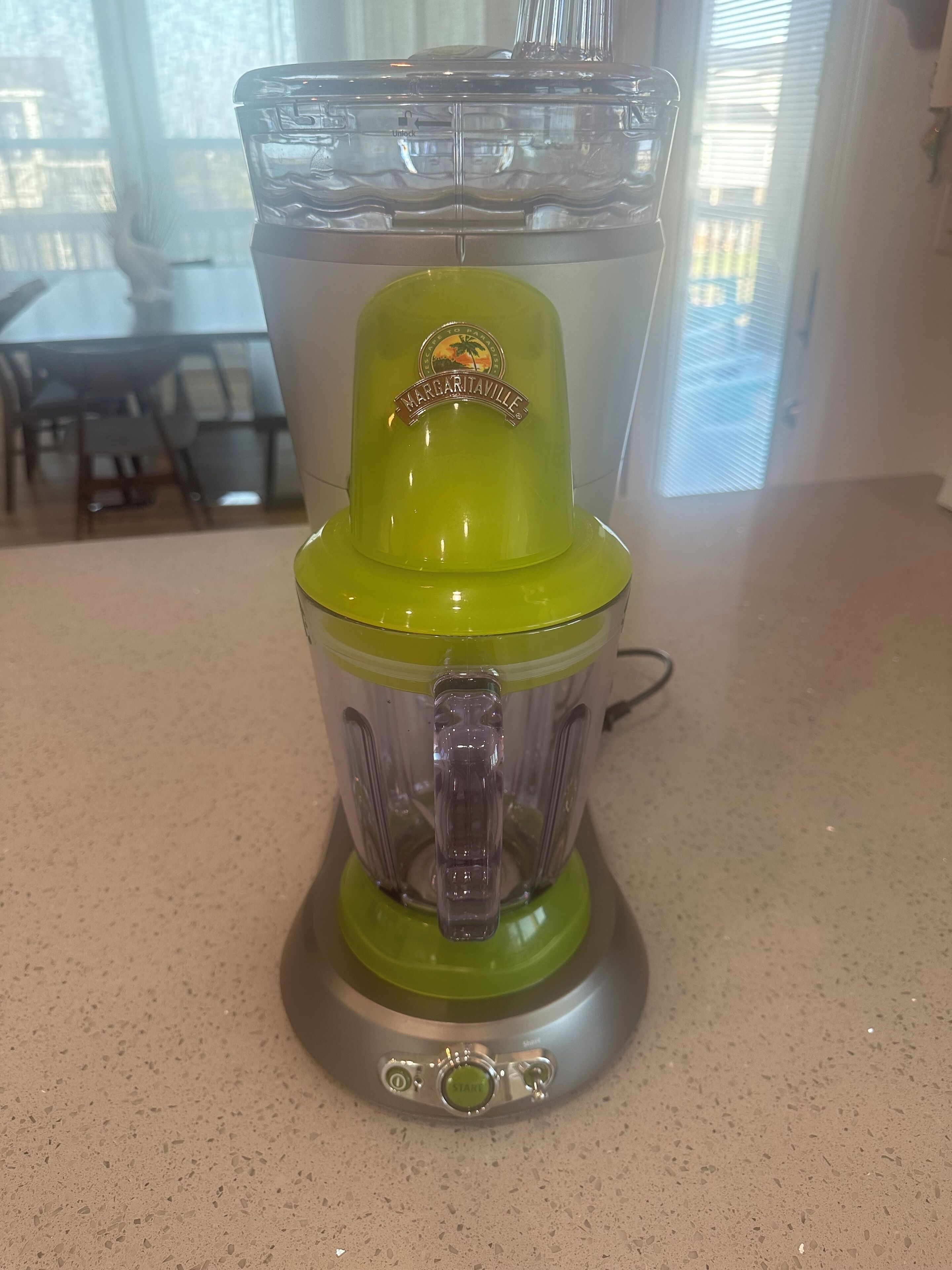 A green and clear blender with a brand label on the top, placed on a kitchen countertop.