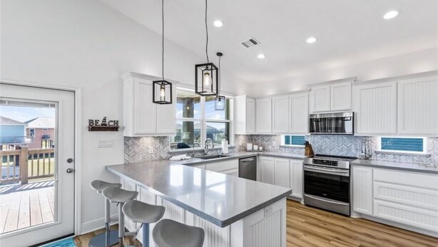 Una cocina moderna con armarios blancos, una isla grande con taburetes de bar, un microondas y un horno.
