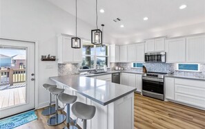 Una cocina moderna con armarios blancos, una isla grande con taburetes de bar, un microondas y un horno.