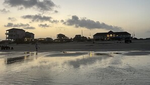 Una playa con casas al fondo y una persona caminando sobre la arena.