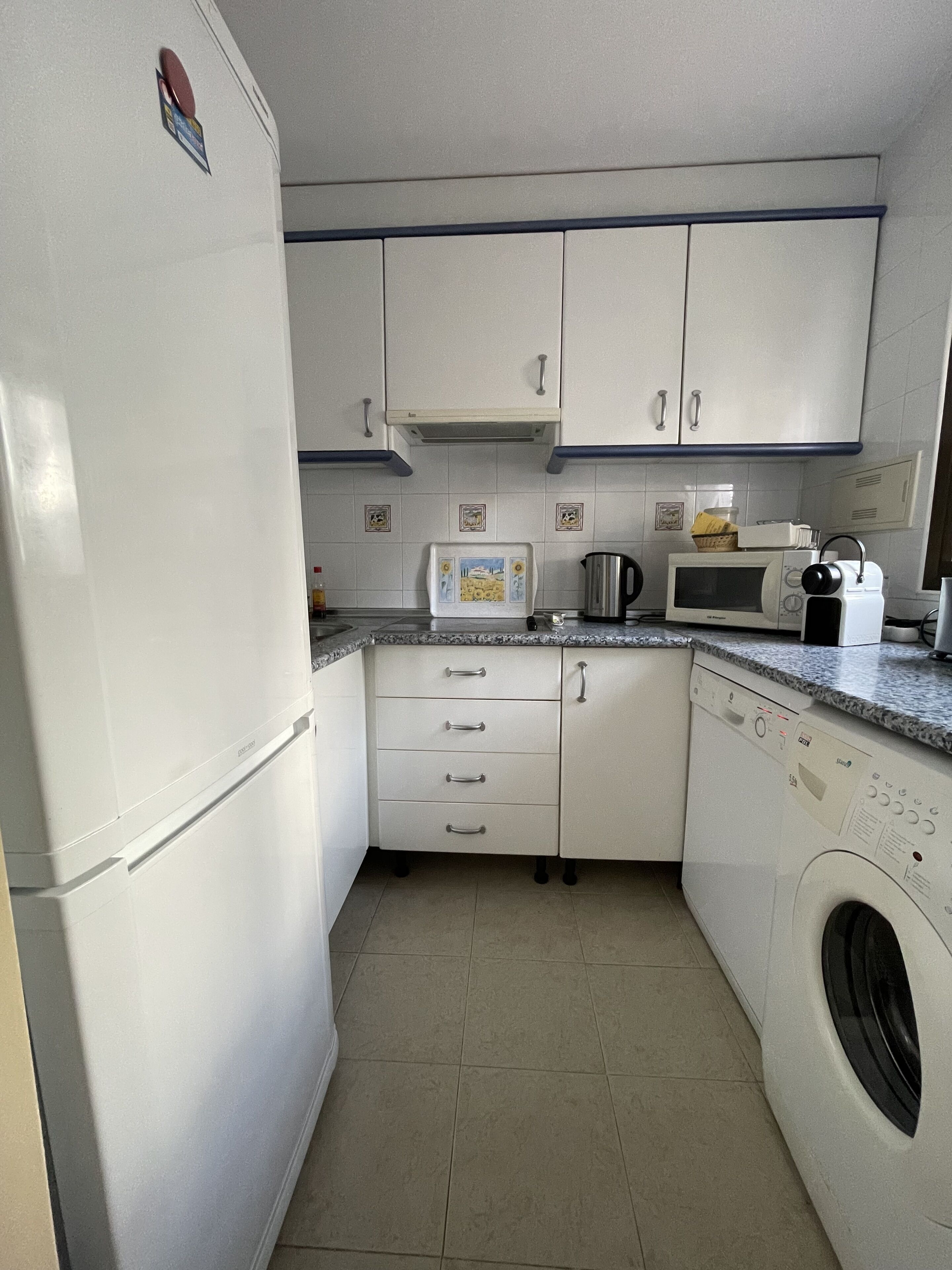 Una cocina compacta con armarios blancos, microondas, lavadora y un lavamanos pequeño.