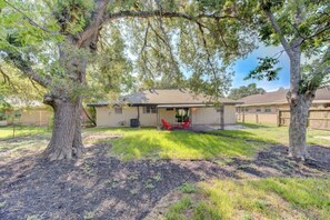 A house with a covered patio, a lawn, and two large trees.