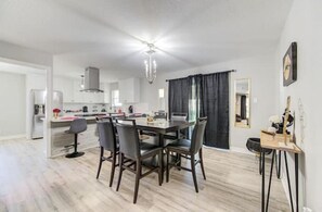 Uma cozinha moderna com armários brancos, um espaço de jantar com mesa e cadeiras de madeira escura e um lustre.