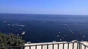 Une vue sur la côte, avec des bateaux sur l’eau, un ciel dégagé et une rambarde au premier plan.