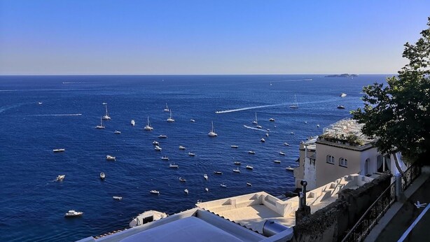 Une vue sur la côte, avec des bateaux sur la mer, des bâtiments dotés de balcons et un ciel dégagé.