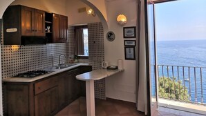 Une cuisine compacte avec vue sur la mer, équipée d’une cuisinière à gaz, d’un évier et d’un petit îlot central.