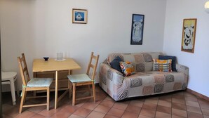 Un salon comprenant un canapé, deux fauteuils, une table à manger et un petit coin cuisine.