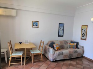 Sala de estar com sofá, duas cadeiras, mesa de jantar e pequena cozinha.