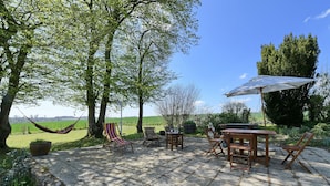 A patio with a table, chairs, a hammock, and a large umbrella.