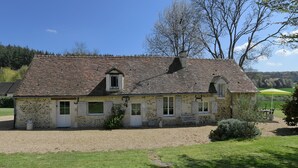 A stone building with a tiled roof, a gravel driveway, and a green lawn.
