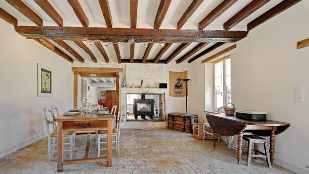 A rustic dining area with a wooden table and chairs, a fireplace, and a stone floor.