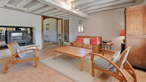 A living room with a wooden coffee table, two rocking chairs, a sofa with patterned cushions, a television, and a wooden cabinet.