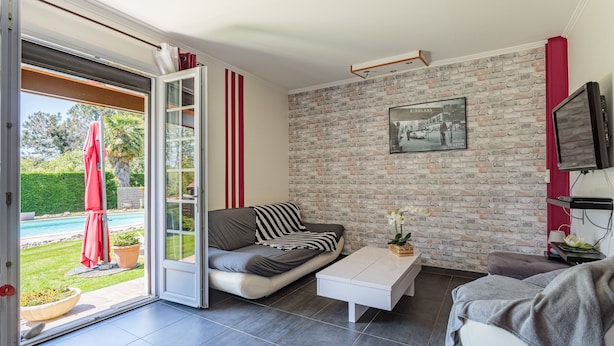Una sala de estar moderna con sofá, mesa de centro y televisor. Unos puertas de cristal dan acceso a una zona de piscina.