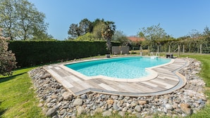 Una piscina rectangular con cubierta de madera, rodeada por un jardín ajardinado con setos y árboles.