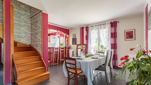 Un comedor con una mesa preparada para cuatro personas, una escalera de madera y vistas a la cocina.