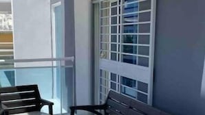A balcony with a sofa and chairs, large windows, and a view of the city. - Cómodo Apartamento en Santo Domingo Este (Santo Domingo Este)