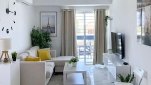 A modern living room with a sofa, coffee table, and a TV. There is a clock on the wall and a plant on the side. - Cómodo Apartamento en Santo Domingo Este (Santo Domingo Este)