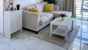 A modern living room with a white sofa, a coffee table, and a large wall clock. - Cómodo Apartamento en Santo Domingo Este (Santo Domingo Este)