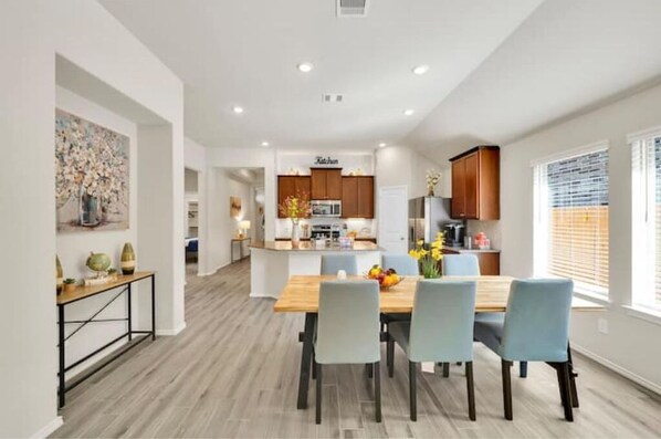 A modern kitchen with wooden cabinets, a central island, and a dining area with a wooden table and four chairs.