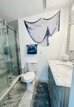 A bathroom with a glass shower enclosure, a toilet, a marble sink, and a decorative net on the wall. - Newly Renovated 3BD/2BTH, 1 BLK to Beach (Brigantine)