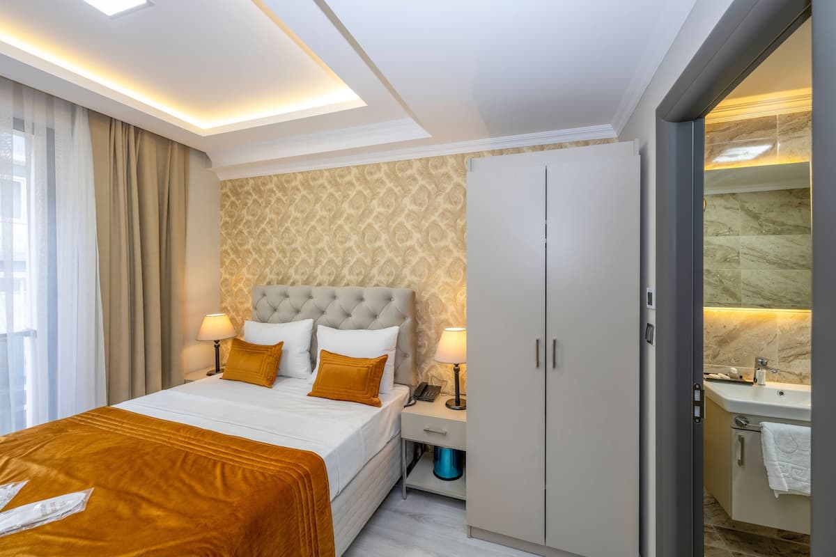 A hotel room with a bed, bedside lamps, a wardrobe, a bathroom with a sink, and a towel rack.
