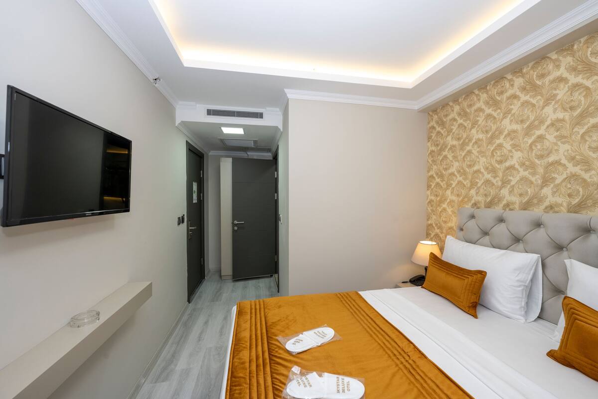 A hotel room with a bed, a television mounted on the wall, a door leading to another room, and a patterned wallpaper on the wall.