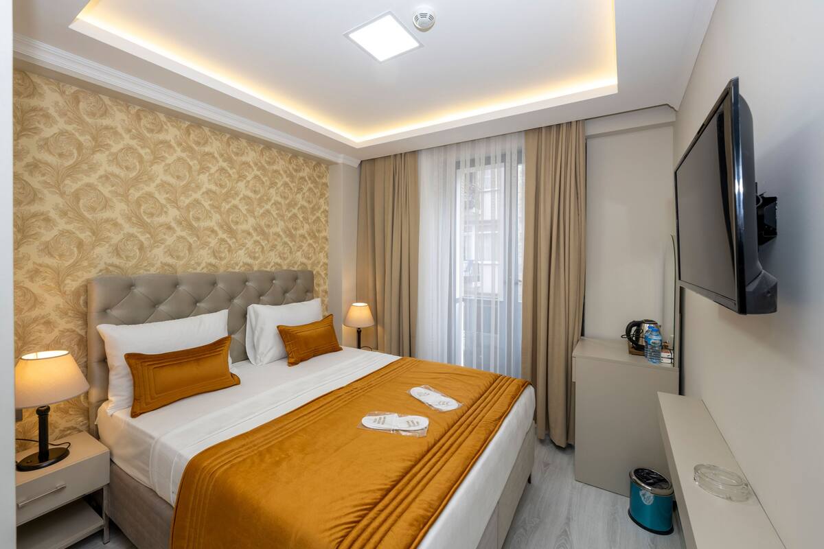 A hotel room with a large bed, a TV, a desk, and a minibar.