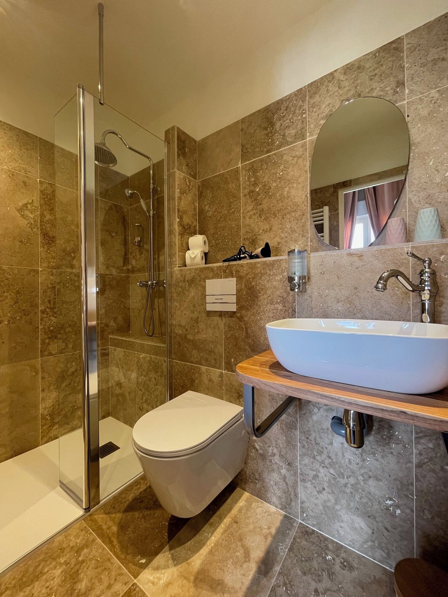 Een moderne badkamer met een glazen douchecabine, een wit toilet en een groot ovaal wastafelmeubel met een houten blad.