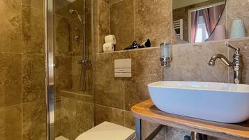 Un baño moderno con ducha de vidrio, inodoro blanco y un lavamanos ovalado grande con encimera de madera.