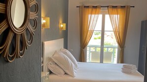 A hotel room with a bed, a nightstand, a mirror, and a window with curtains. - Hôtel Michelet Plage (Soulac-sur-Mer)