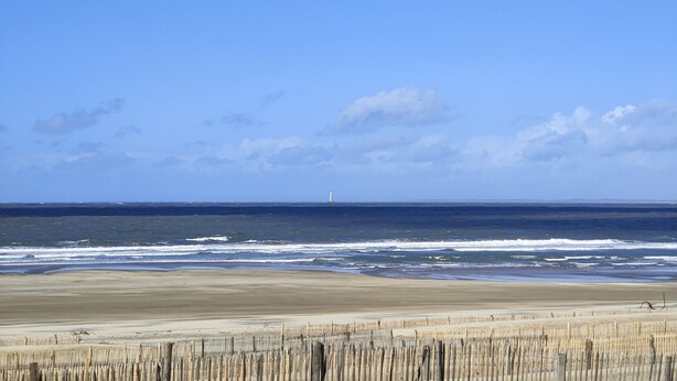 A beach with a wooden fence in the foreground and a lighthouse in the distance. - Hôtel Michelet Plage (Soulac-sur-Mer)