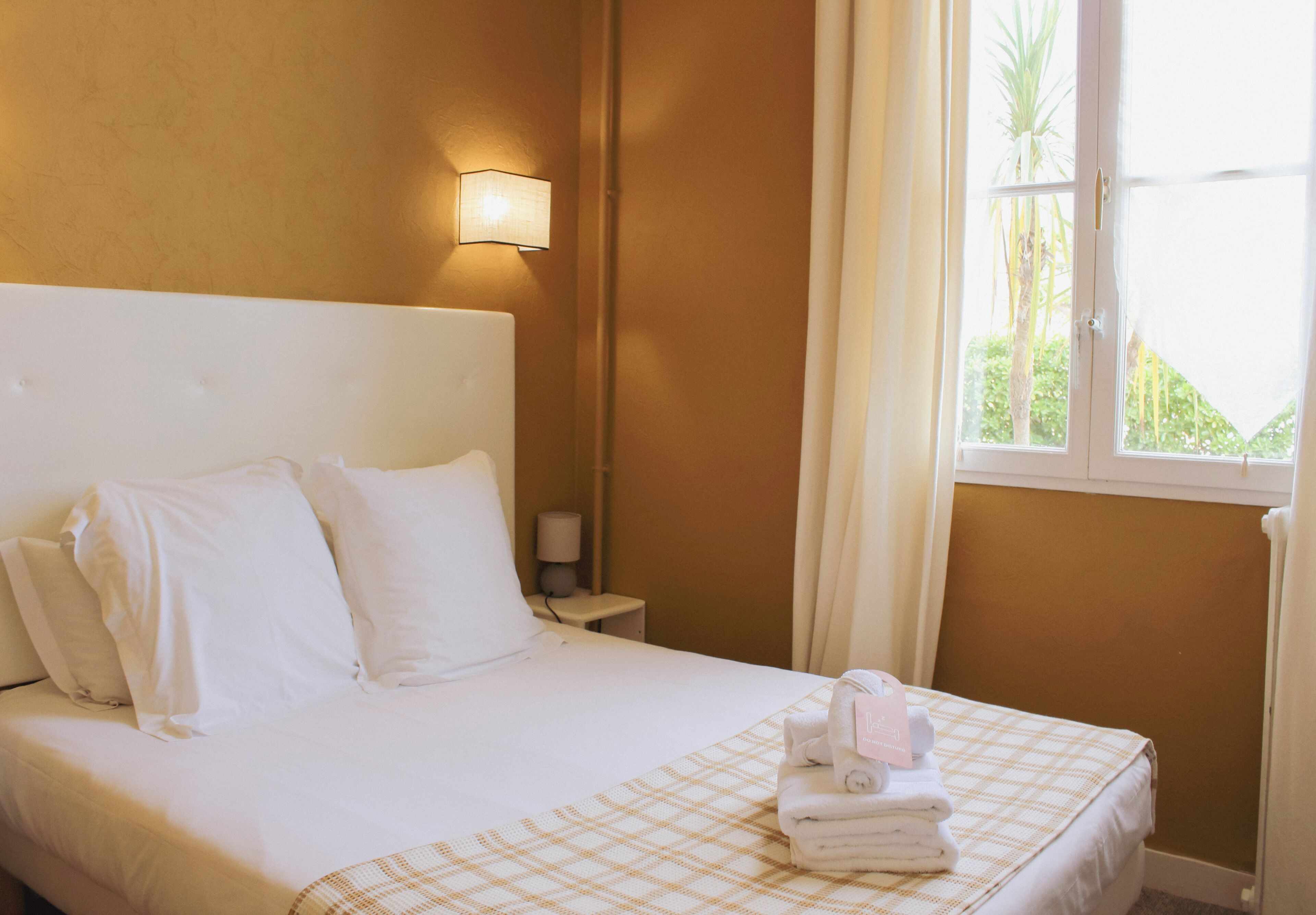 A hotel room with a bed, a nightstand, a lamp, and a window with curtains.