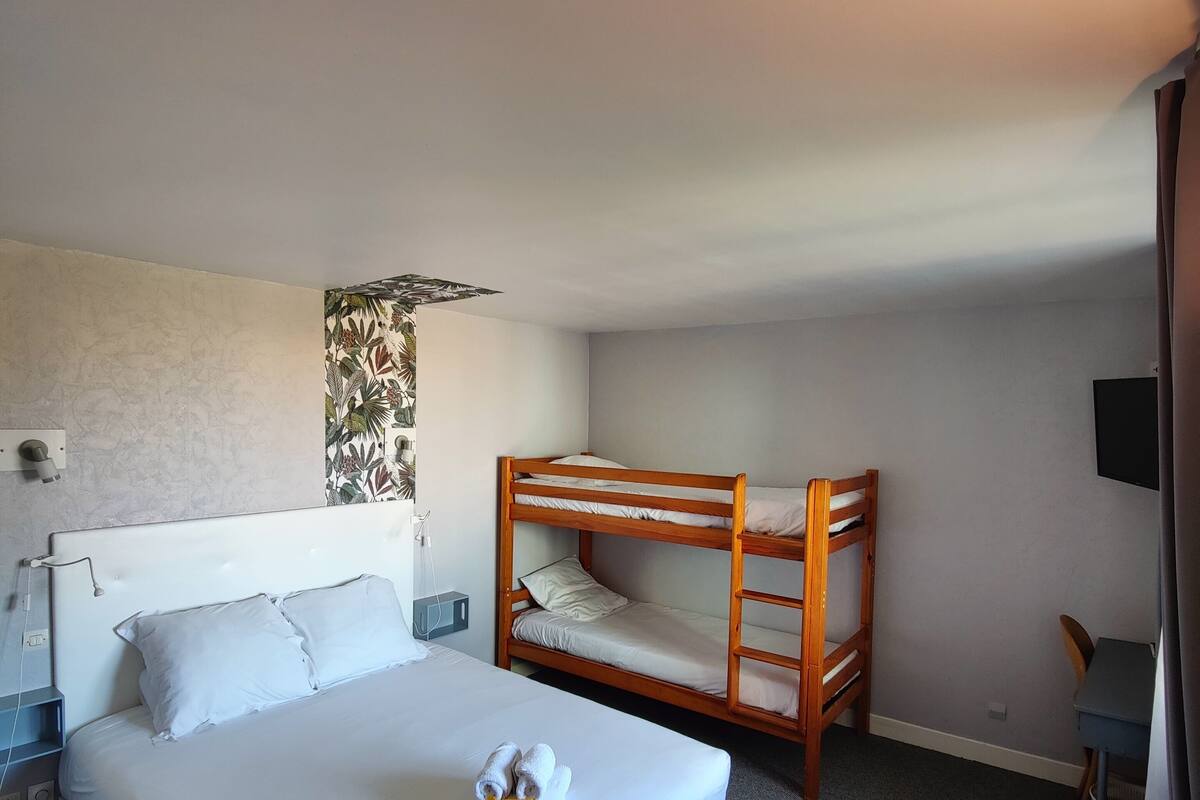A hotel room with a single bed, a bunk bed, a desk, a chair, and a TV.
