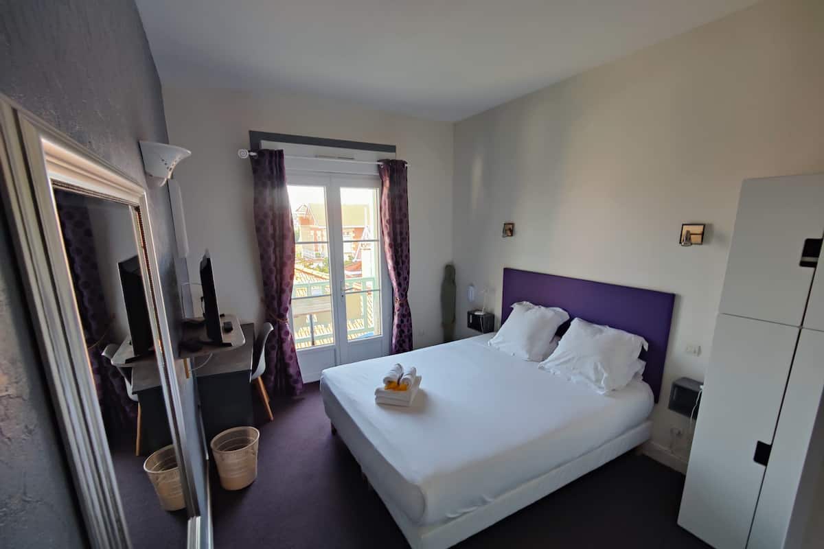 A hotel room with a large bed, a desk, a chair, a wardrobe, and a window with curtains.