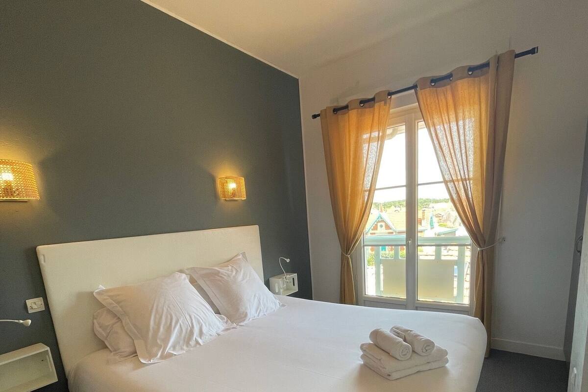 A hotel room with a large bed, two bedside lamps, a window with curtains, and a view of the outside.
